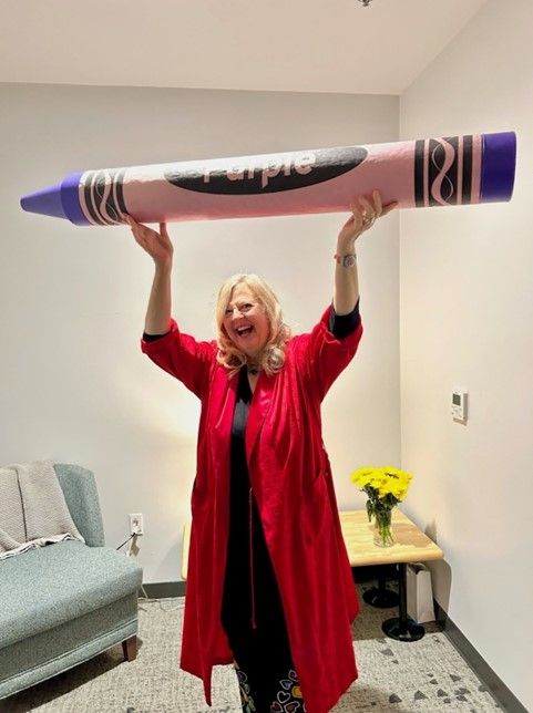 SARK holds a giant purple crayon over her head with excitement