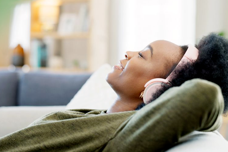 Woman reclining on a couch wearing headphones, listening with her eyes closed