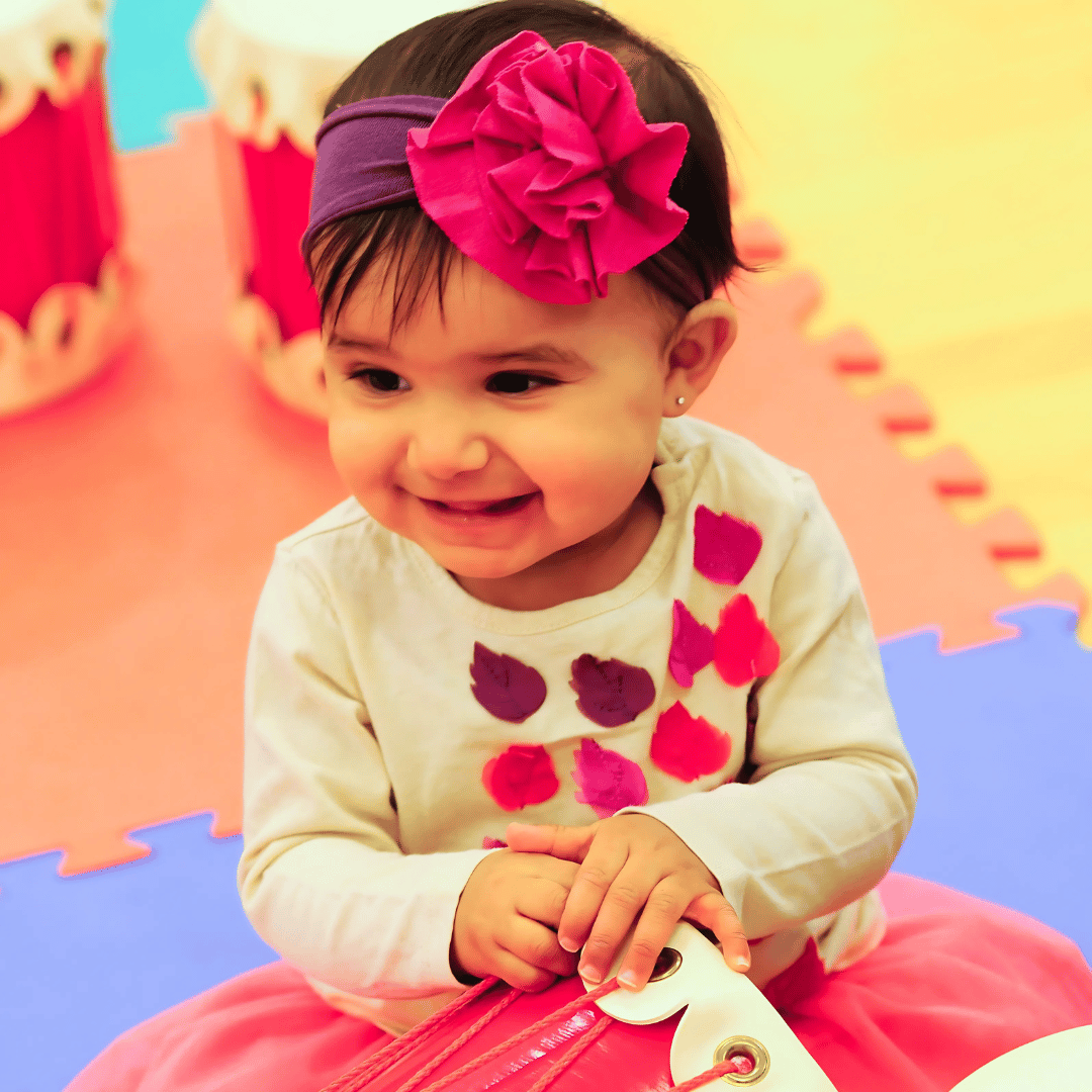 A toddler girl is smiling and holding a toy drum.