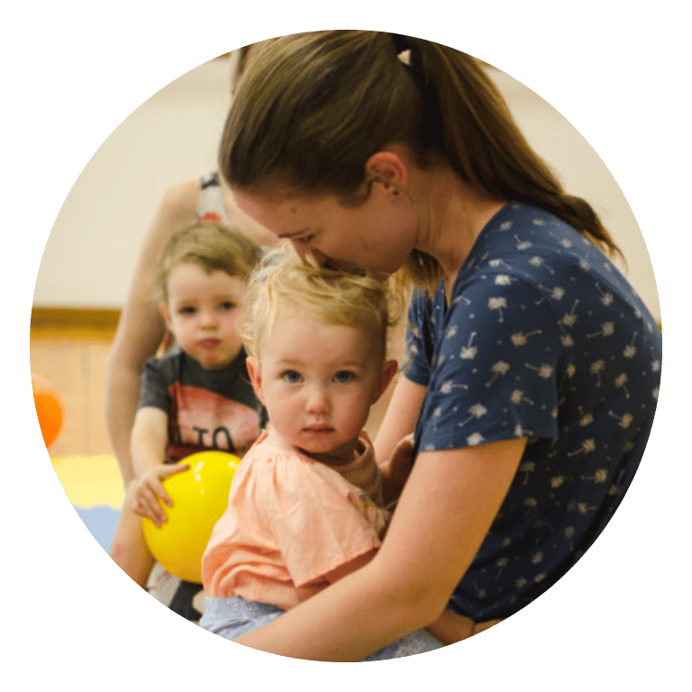 A mom and toddler boy are sitting on the floor snuggling.
