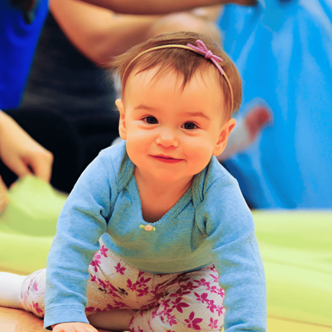 A baby girl is crawling and smiling.