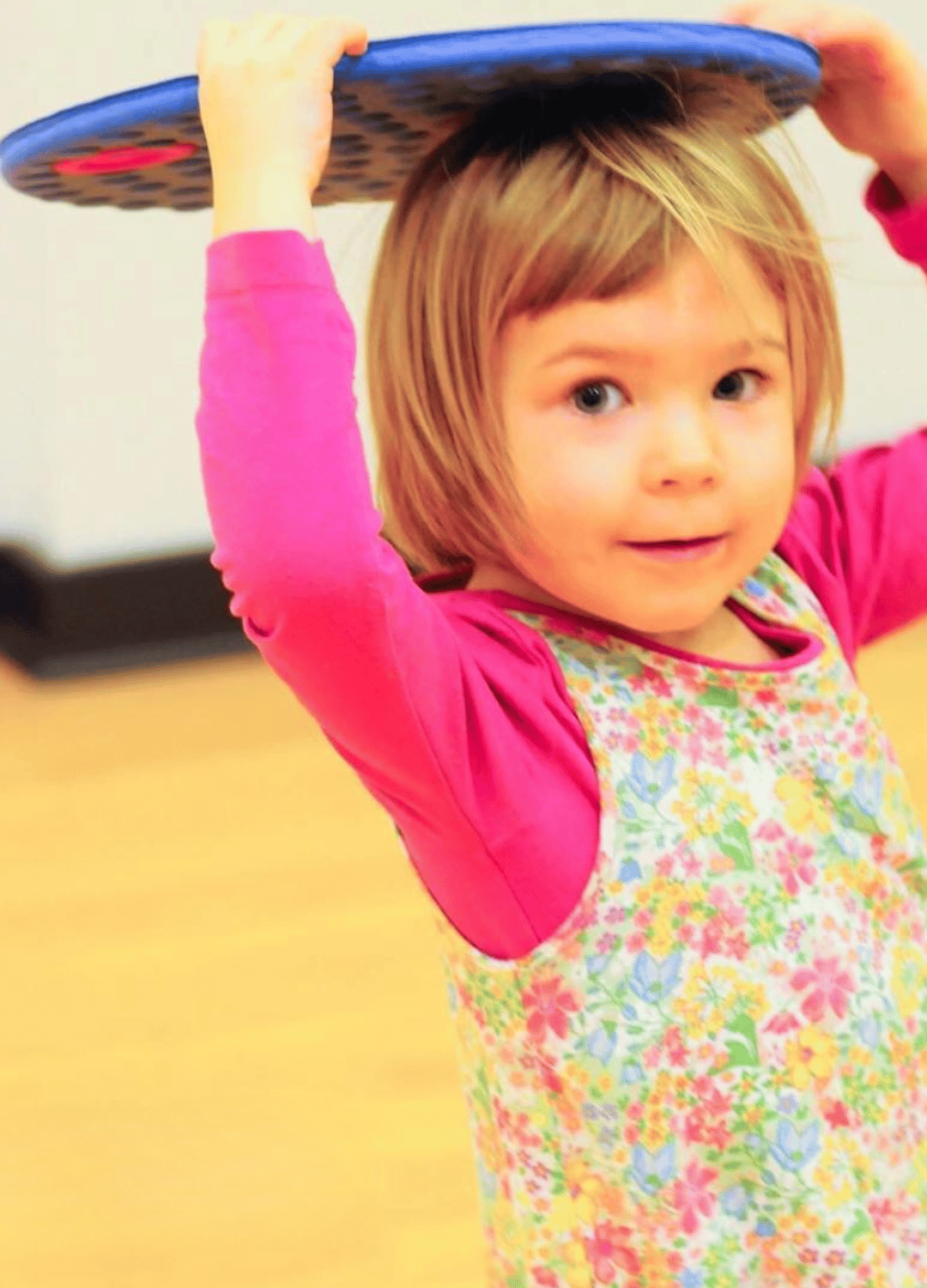A preschool aged girl is standing holding a floor dot over her head.