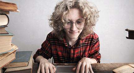 A nerdy guy infront of his laptop while having a lot of books on the side