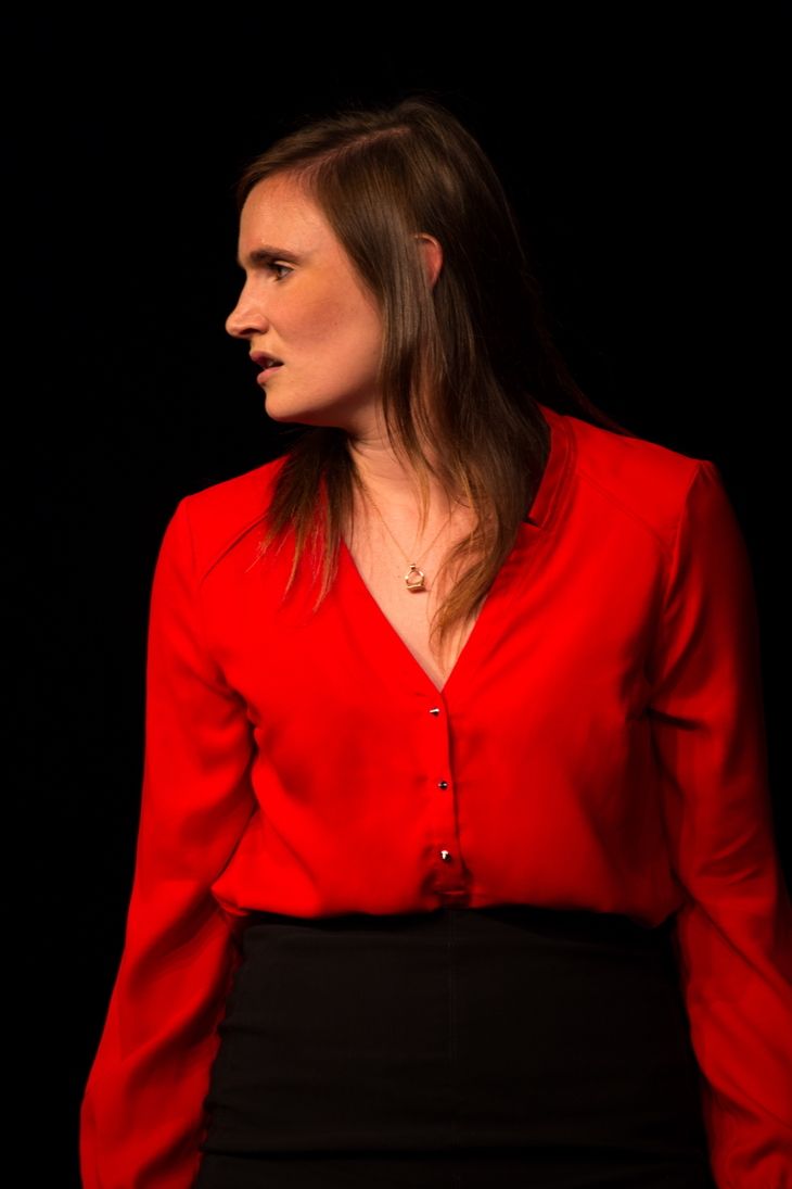 Female actor on stage wearing red blouse and black skirt