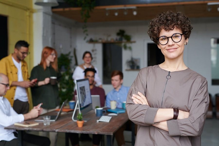 A woman with glasses standing confidently in front of a diverse group of people.