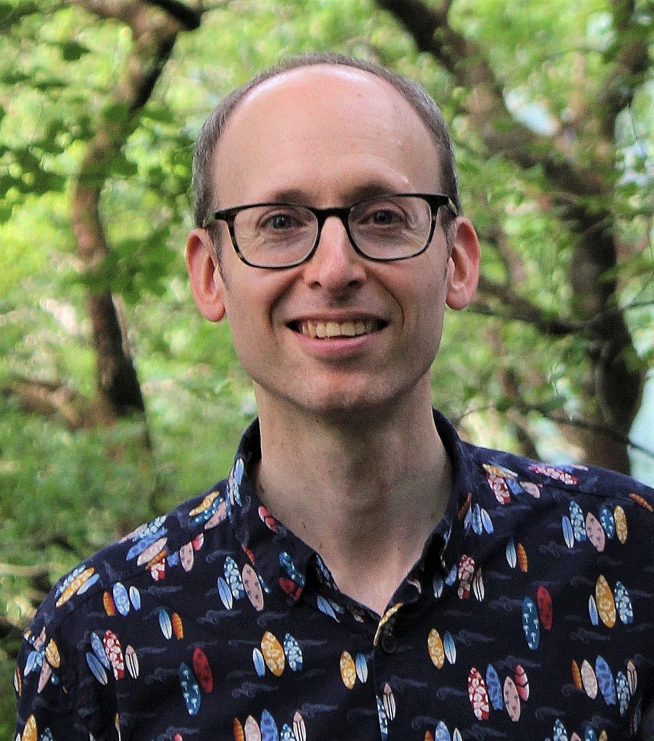 Marc Harris - A smiling white guy with eyeglass wearing a blue patterned polo in a