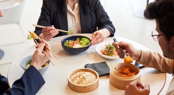 Three people dining on a circular table while eating salad