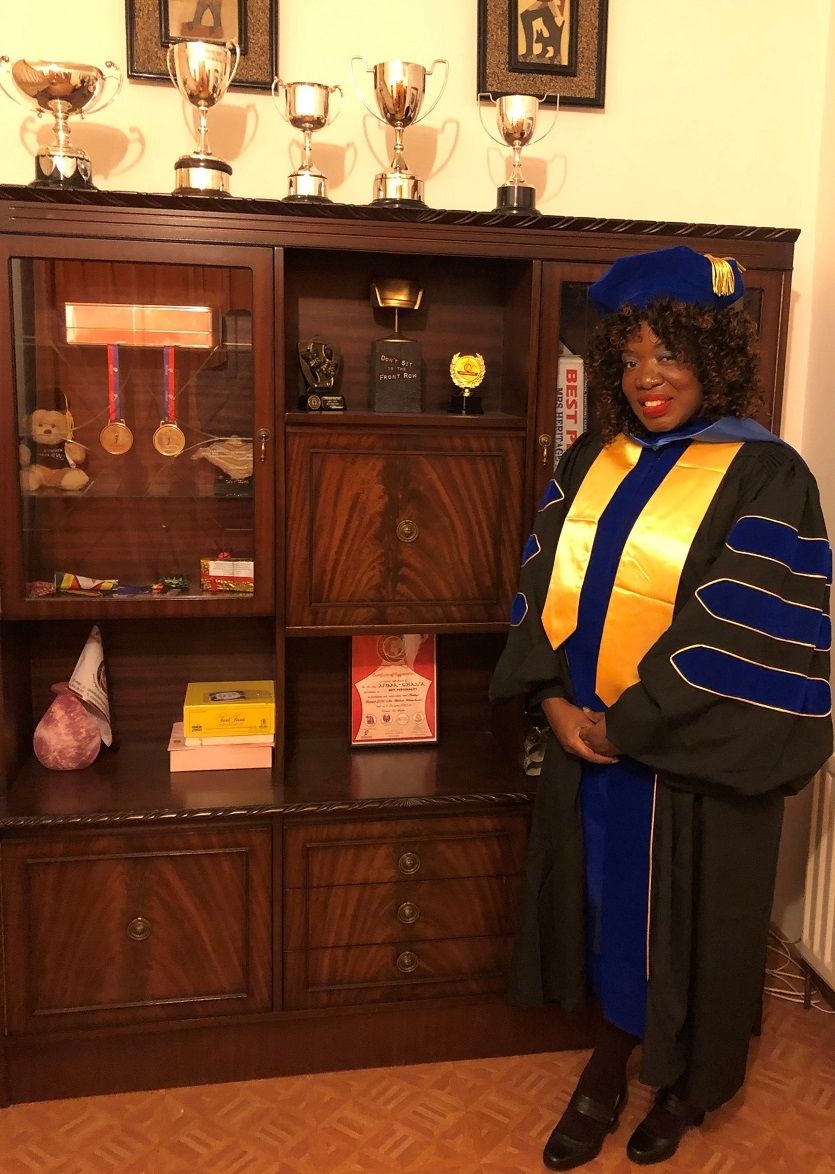 Nyaka Chana wearing a black toga standing in front of an apparatus of trophies and medals