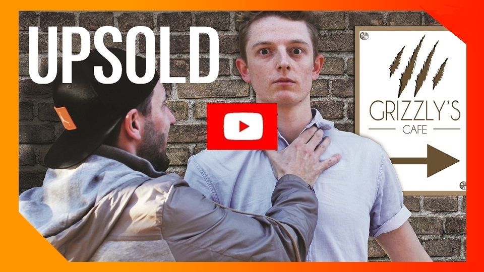 A male wearing a cap violently pushing another man towards the wall with a sign that says the direction on where the Grizzly's cafe is