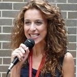 Katherine Babatzanis - a Blonde girl with a curly hair wearing a black sleeveless shirt while holding a microphone
