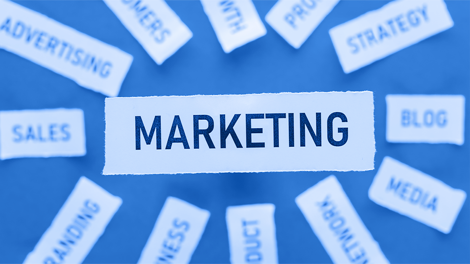 A paper with text that writes "MARKETING" surrounded by papers with branches of Marketing