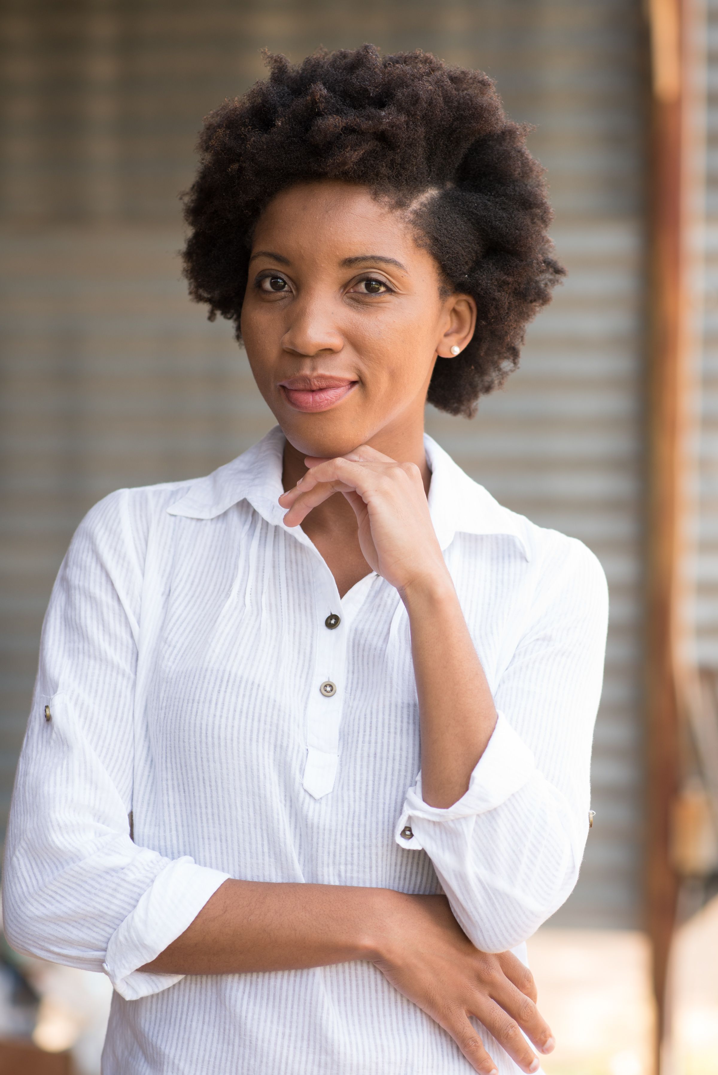 Jane Mpholo, a curly haired woman wearing a white blouse posing infront of a camera