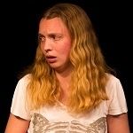 Portrait of Sarah North with blonde hair and wearing a white blouse on a black background