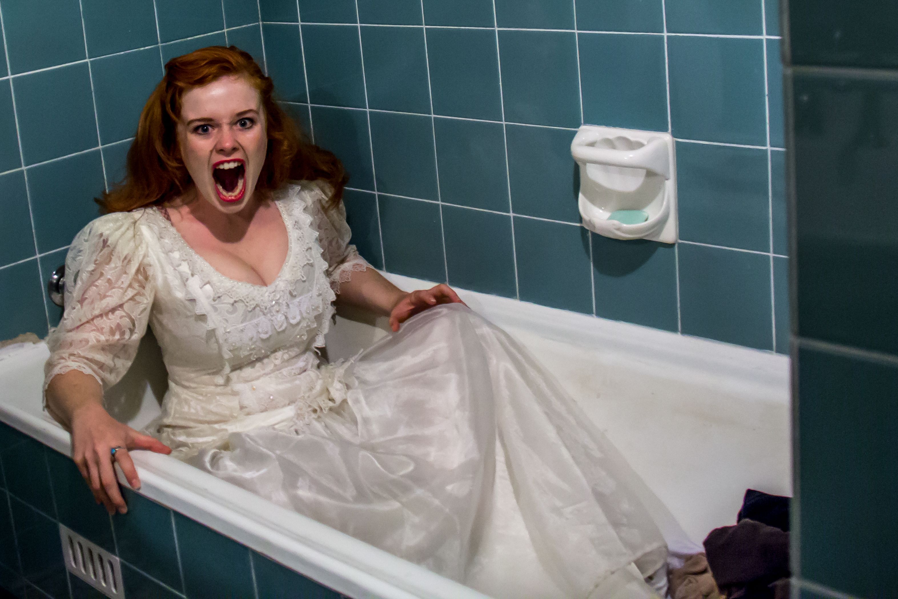 Ginger Female with open mouth wearing white dress in a bathroom inside a bath tub