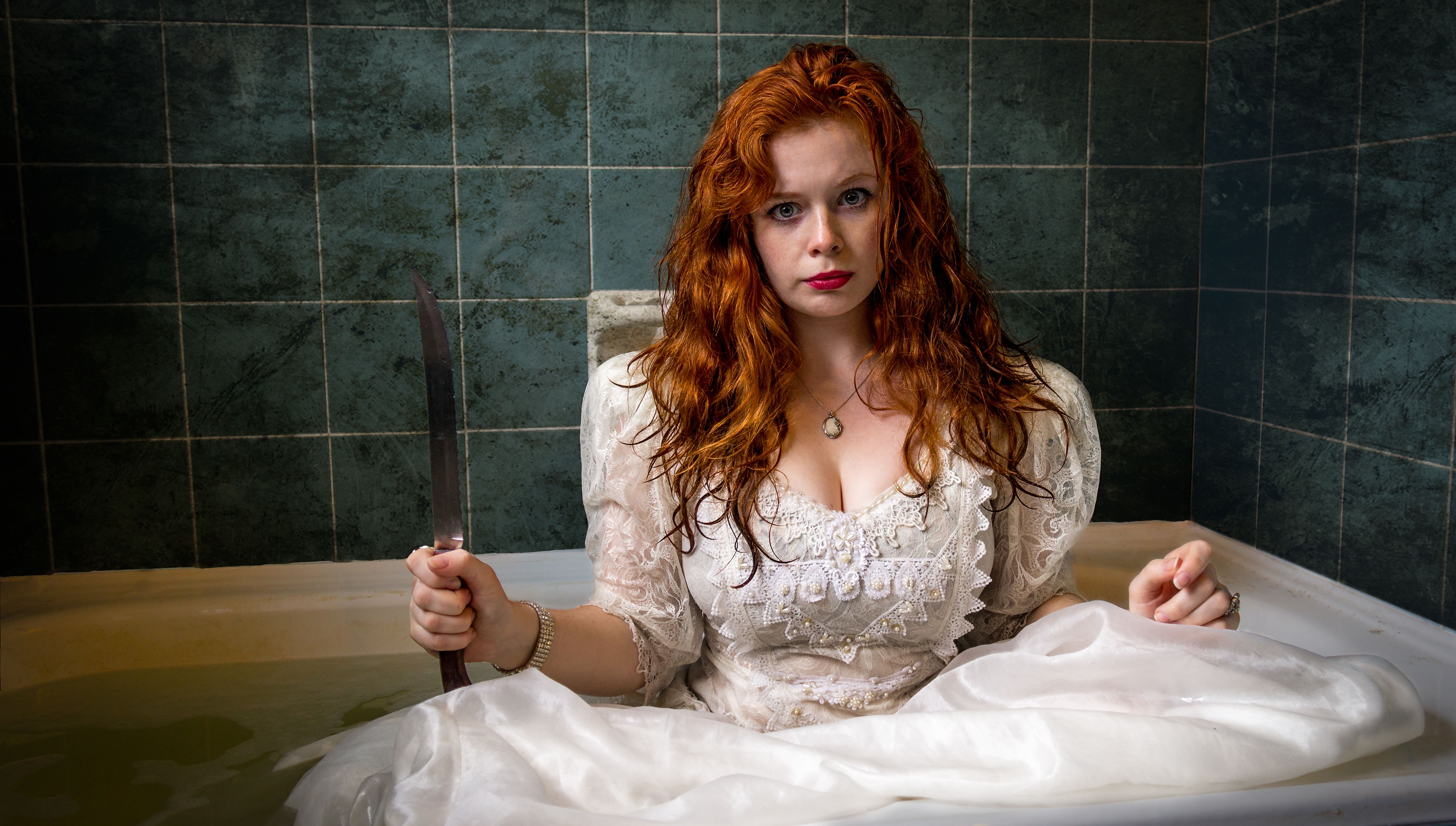 Ginger Female wearing a white dress in a bath tub while holding a knife
