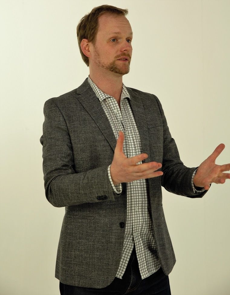 Pete Malicki - A professional man in formal attire making a gesture.