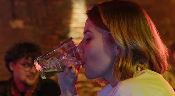 A blonde girl in a bar drinking a glass of liquor