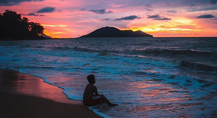 A man sitting in the seashore while watching the sunset