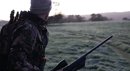 A hunter in the wild holding his rifle and carrying his equipments
