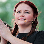 Portrait of Ebony Halliday clapping her hand and a lapel mic on head with a green background