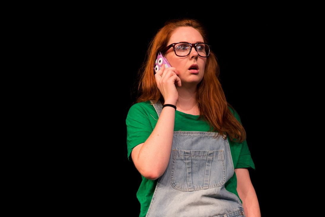 Female Blonde wearing a glasses and green shirt with a jumper doing a call with a cellphone