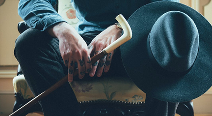 A man sitting holding his baton and Panama hat