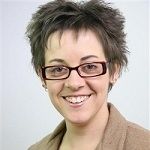 Roz Hicks - A gray short haired girl wearing eye glasses and brown jacket