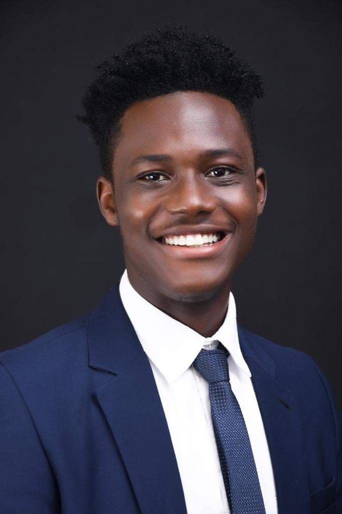 Charles Telus - A smiling black guy wearing a navy blue coat and tie with an afro haircut