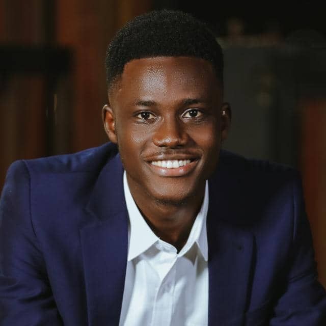 Charles Telus - A smiling black guy wearing a navy blue coat and tie with an afro haircut