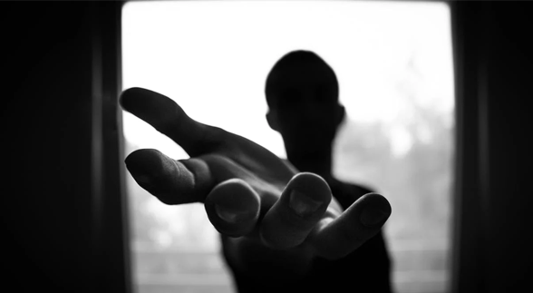 A black and white image of a faceless male reaching out his hands for help