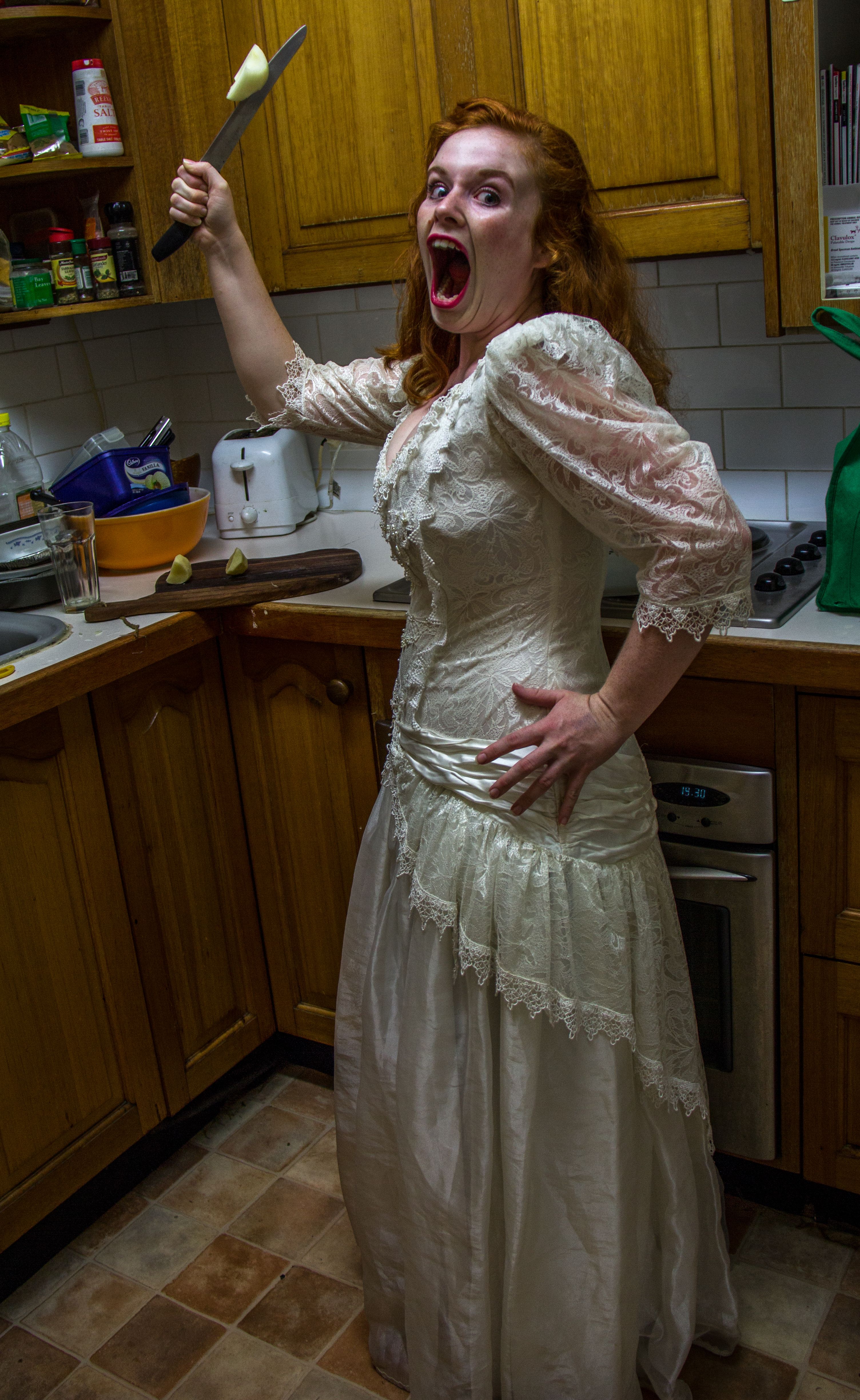 Ginger Female wearing a white dress in a kitchen holding a knife
