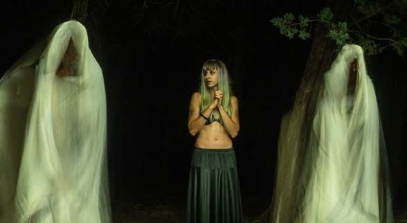 A green haired woman wearing a black skirt surrounded by ghosts