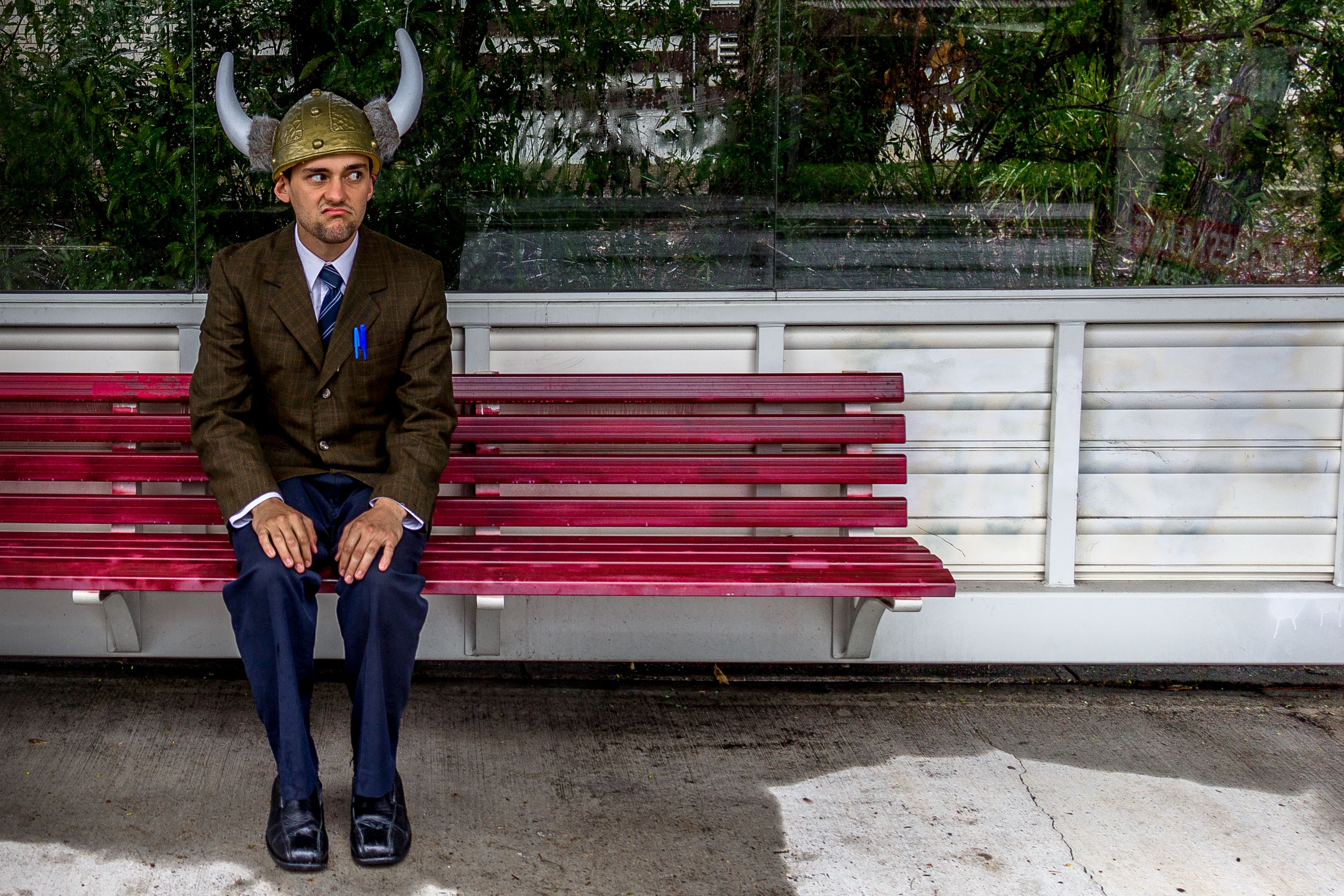 Guy sitting on a red bench wearing a brown coat and a barbarian helm