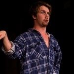 Portrait of Nat Backhouse doing a hand gesture acting on stage doing a funny face on a black background