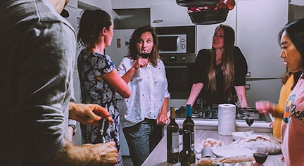 A group of friends gathering in the kitchen while drinking wine and talking to each other