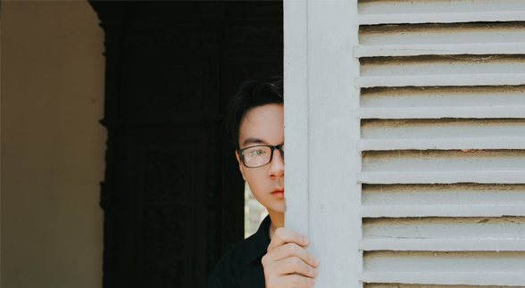 A male peeking half-face behind a window