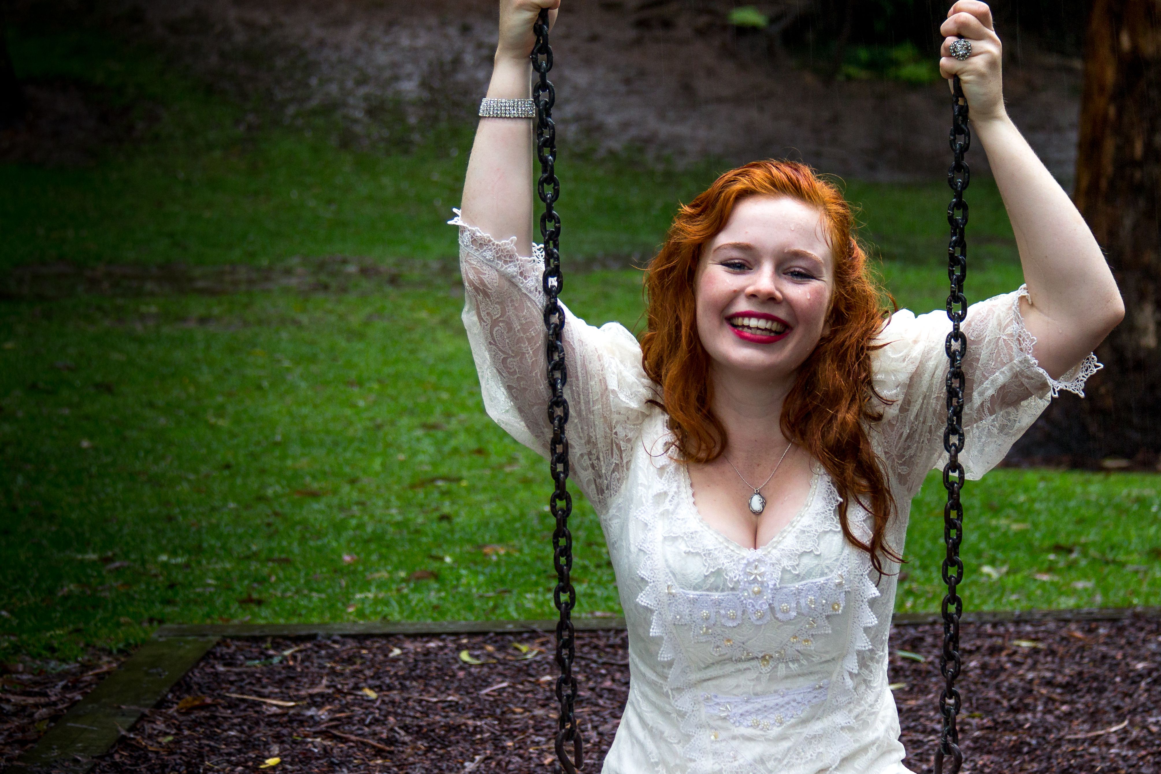 A smiling Ginger Female at a park riding a swing 