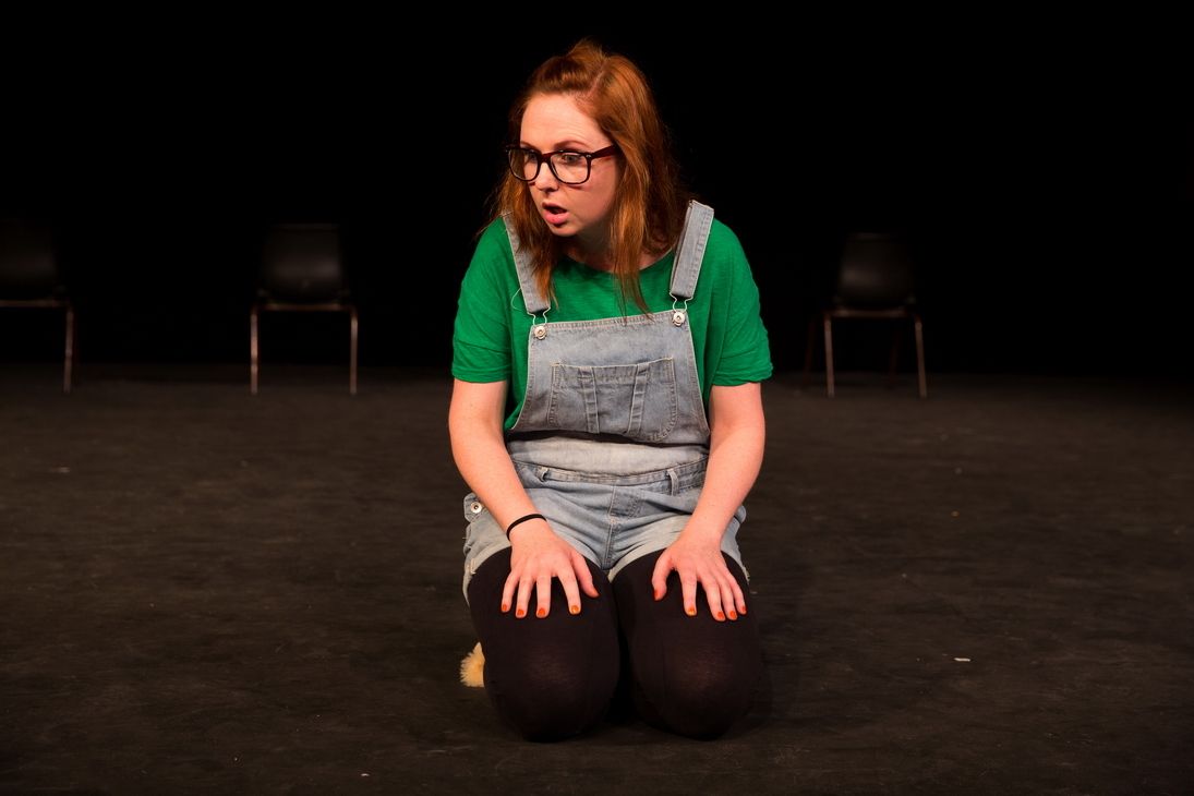 Kneeling blonde girl wearing a glasses, green shirt with a jumper and a brown boots