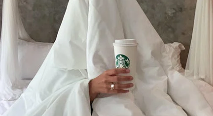 A man under the blanket holding a cup of starbucks coffee