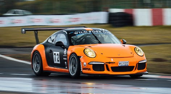 An orange with black tracings porsche boxster in a race track