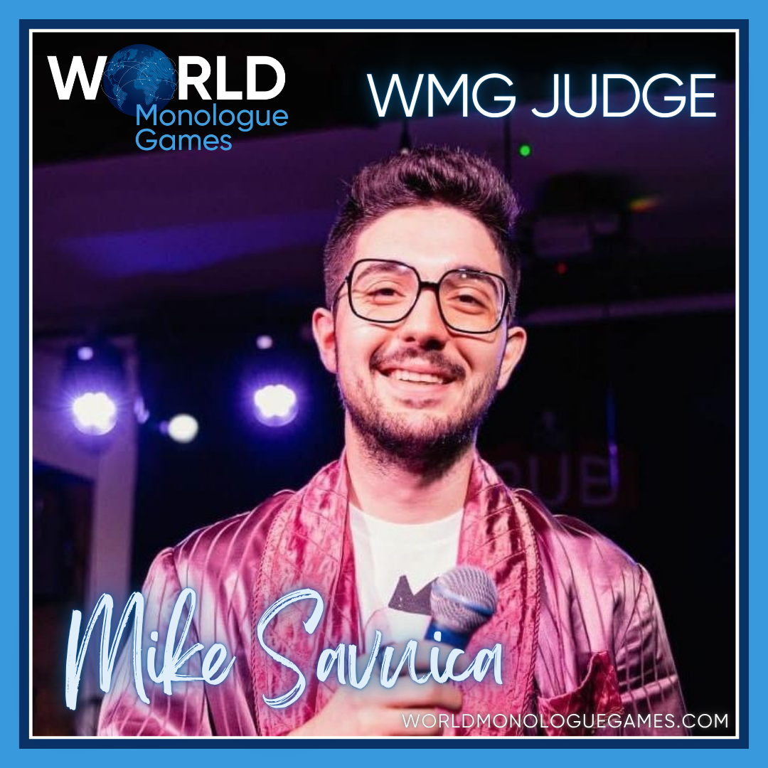 Mike Savuica - A cool bearded guy wearing a glasses, pink coat and white shirt in the inside while holding a microphone