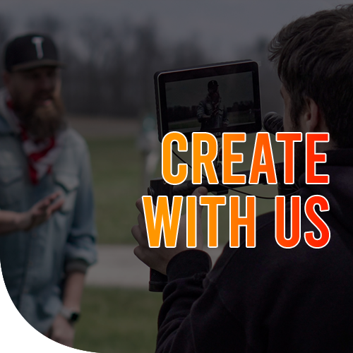 A male filming a bearded guy wearing a cap and a denim jacket in a park