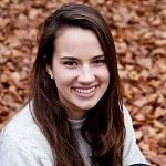 Davita van der Velde - A woman with a long brown hair, smiling and wearing a white sweatshirt