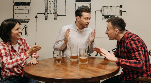 Two male and 1 female sitting on a round table and drinking beer