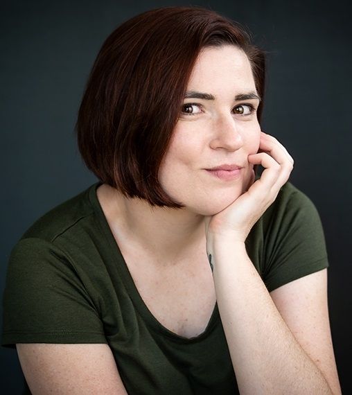 Faeron Wheeler - Portrait of a woman in a green shirt and short hair, looking cheerful.