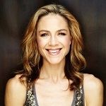 Jusine Scali - A woman with a Golden hair, wearing a big smile and a black patterned dress