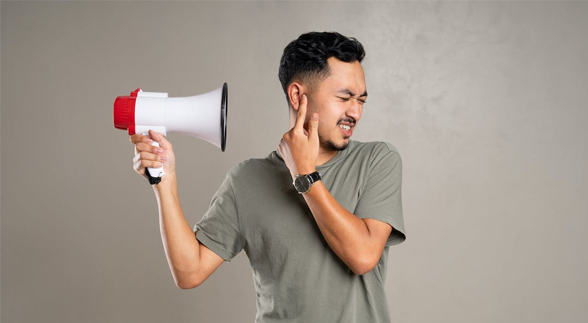 Male holding a megaphone while he cover his ears