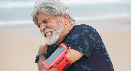 An old guy looking in pain while jogging in the beack