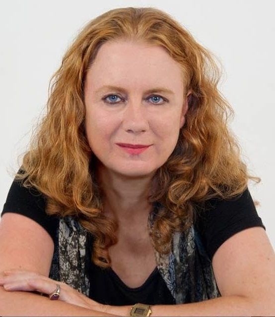 Luci Lenox - A blonde woman wearing a black shirt and a textured scarf with a ring and gold watch