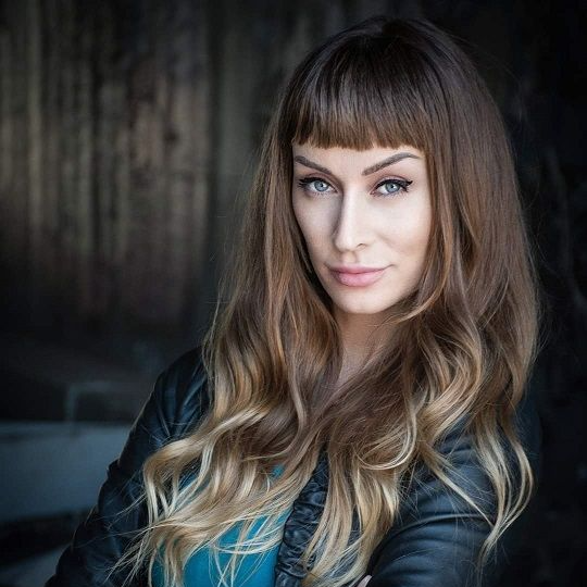 Nea Dune, A fierce woman with a blonde hair and a straight bangs wearing a leather jacket with blue shirt in the inside